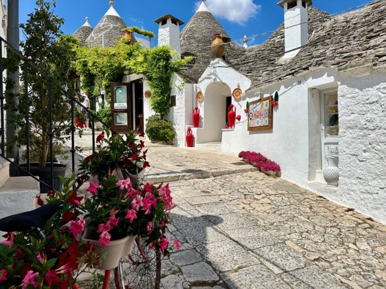 Quaint sidewalk through the Trulli of Alberobello, Italy lined with flower pots filled with pink flowers