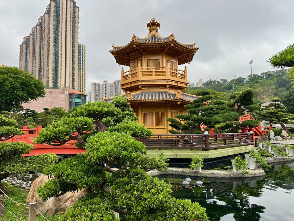 View of a temple in Hong Kong's Nan Lian Garden surrounded by trees with towering high rise building in the background.